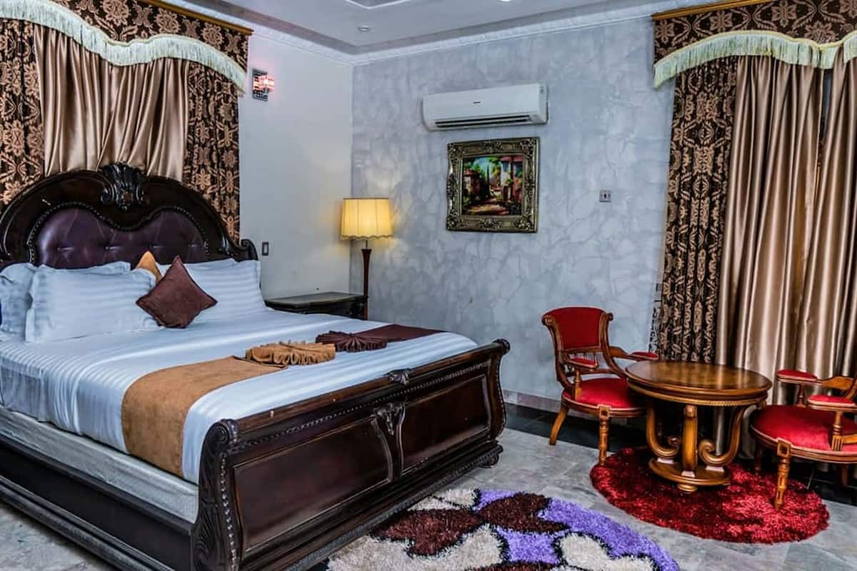A hotel room with a large bed, a bedside table with a lamp, a small round table with chairs, and a painting on the wall.
