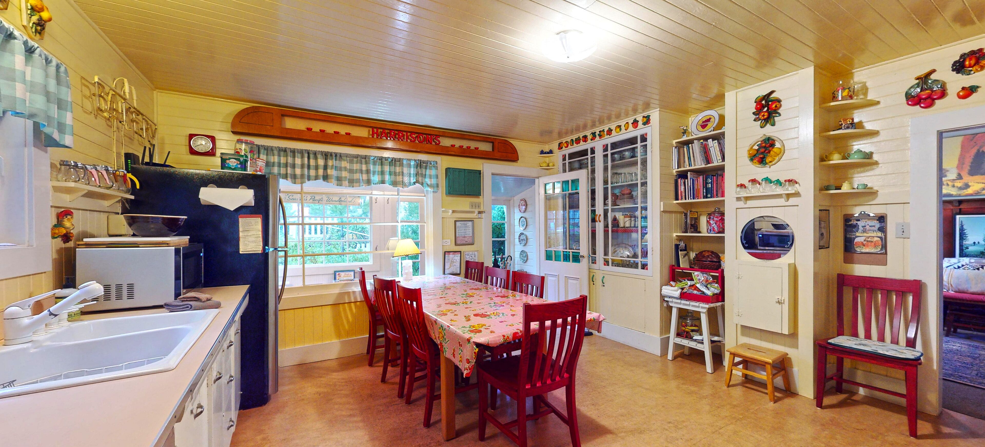 A kitchen with a dining table, chairs, a refrigerator, and a window.