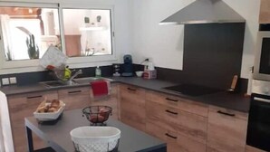 A modern kitchen with wooden cabinets, a central island with a sink, and a stainless steel range hood. - Welcome to Villa Bergeracoise - Les Cigales. (Eyraud-Crempse-Maurens)