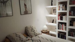 A bedroom with a bed, pillows, a bedside table with a lamp, and a bookshelf filled with books. - Welcome to Villa Bergeracoise - Les Cigales. (Eyraud-Crempse-Maurens)