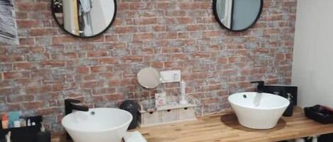 A bathroom with a brick wall, two round mirrors, a clock, and a wooden vanity with two sinks.