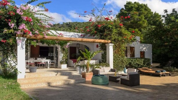 Una casa amb un pati, seients a l'exterior i un jardí amb plantes florents.