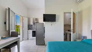 A modern hotel room with a bed, a desk, a chair, a flat-screen TV, a kitchen area, and a bathroom. - 3771 Villino Cento Passi by Barbarhouse (Nardò)