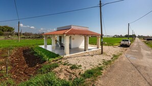 A small, open pavilion with a tiled roof, surrounded by a dirt path and green fields, with a white pickup truck parked nearby. - 3771 Villino Cento Passi by Barbarhouse (Nardò)