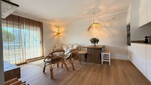 Una cocina moderna con piso de madera, un comedor con sillas de mimbre y un ventanal con persianas.