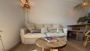 Una sala de estar acogedora con una mesa de centro redonda de madera, un sofá color beige con varios cojines y una pequeña mesita auxiliar de madera.