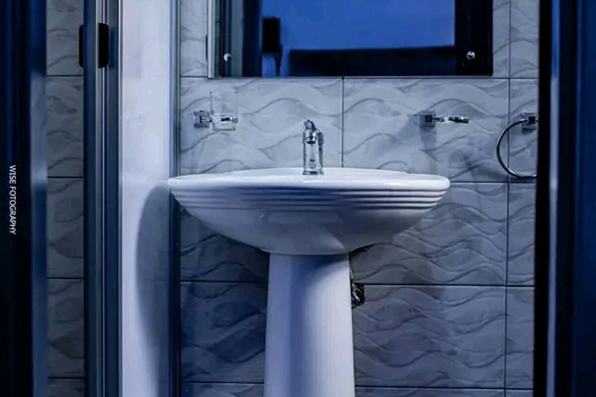 Un baño con un lavamanos pedestal blanco, un espejo encima y un salpicadero de azulejos.