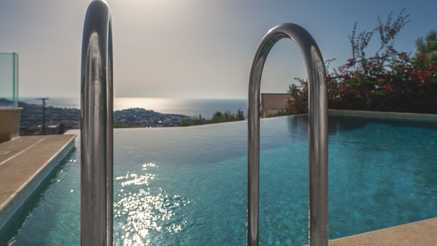 A swimming pool with metal handrails, clear water, and a view of a distant landscape.