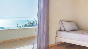 A balcony with a view of the sea, a white sofa with cushions, and a sheer curtain partially drawn.