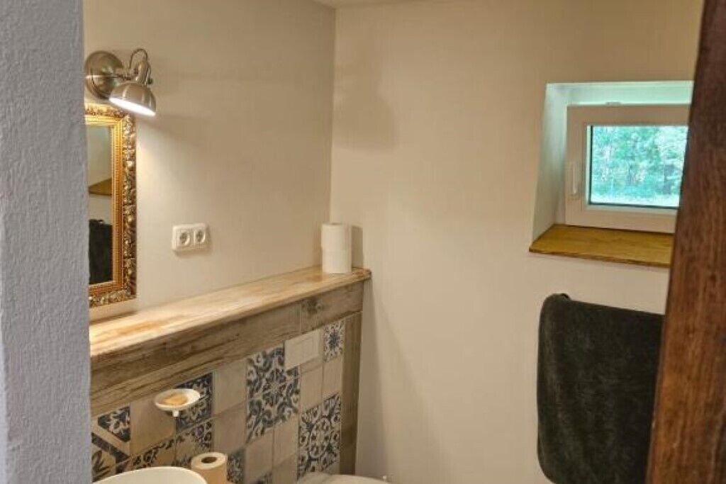 A bathroom with a tiled backsplash, a mirror with a gold frame, a towel hanging on the wall, and a window above the sink.