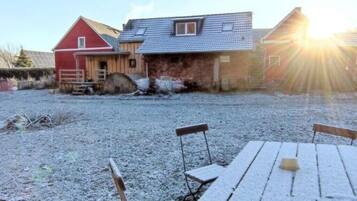 A barn with a red exterior and a wooden door, a gravel driveway, and a picnic table with benches.