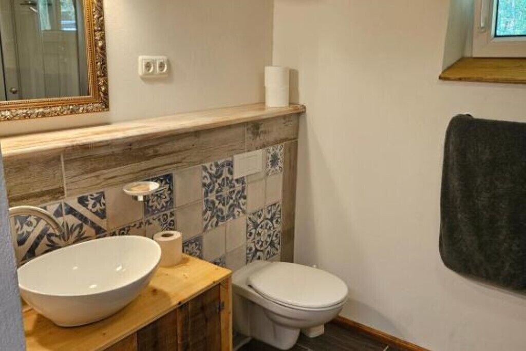 Ein Badezimmer mit einem Holzkosmetikschrank, einem großen weißen Waschbecken, einer Toilette und Wandfliesen mit Muster.