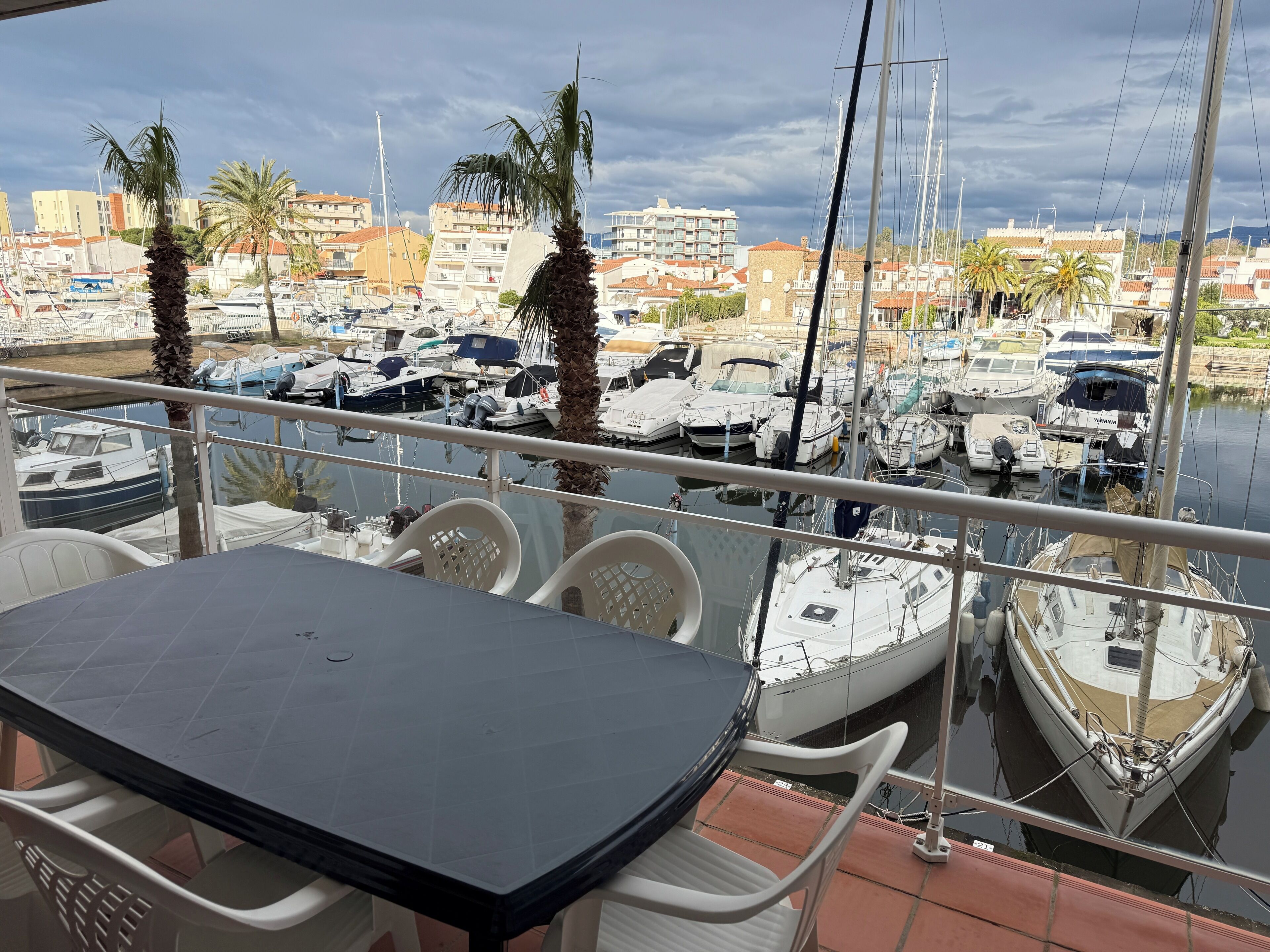 A balcony with a table and chairs overlooking a marina with various boats.