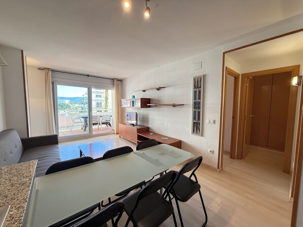 A modern apartment with a dining area, kitchenette, and a balcony with a view of buildings and greenery.