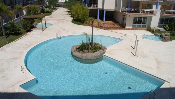 A swimming pool with a circular island in the center, surrounded by a deck area with lounge chairs and a small garden. - Agi Port Canigo 206 Apartamento for rent in Roses Girona. (Roses)
