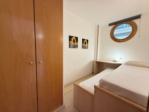 A bedroom with a wooden wardrobe, a bed with a white mattress, a bedside table, a mirror, and two sunflower paintings on the wall.