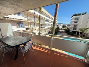 A balcony with a table and chairs, overlooking a swimming pool and a residential area with multiple buildings.