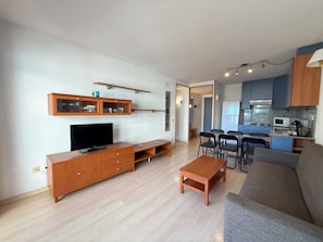 A modern living room with a flat-screen TV, wooden entertainment unit, and a grey sofa.