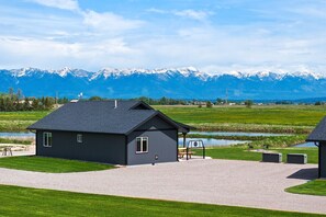 A modern building with a dark exterior, a gravel driveway, and a grassy area with a bench. - Family Friendly Cabins w/ Mountain & Wildlife View (Kalispell)