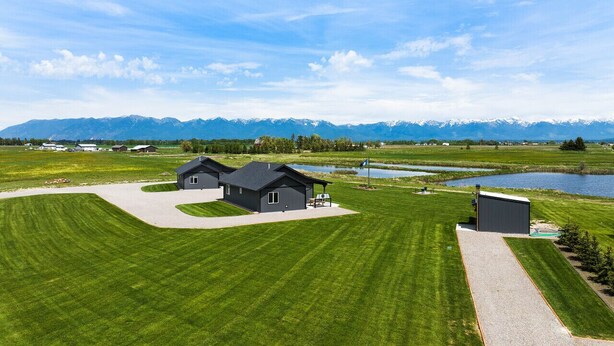 A modern house with a well-maintained lawn, a small pond, and mountains in the background. - Family Friendly Cabins w/ Mountain & Wildlife View (Kalispell)