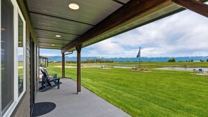 A covered patio with a view of a grassy area, a pond, and mountains in the background. - Family Friendly Cabins w/ Mountain & Wildlife View (Kalispell)