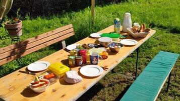 Une table de pique-nique en bois, installée à l’extérieur, sur laquelle on a disposé divers aliments et condiments.