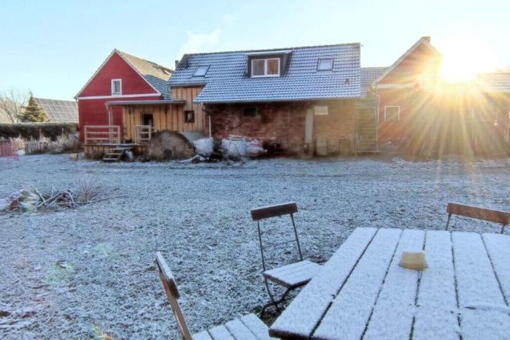 Punaisella maalilla maalattu navetta, jossa on puinen ovi, sorapäällysteinen ajotie ja piknikpöytä penkkeineen.