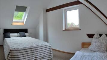 Une chambre avec un plafond en pente, un lit recouvert d’une couvre-lit à rayures, un plus petit lit avec une couvre-lit à motifs floraux, et deux fenêtres qui laissent entrer la lumière naturelle.