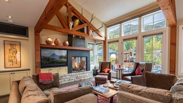 A cozy living room with a fireplace, comfortable seating, and large windows offering a view of the outdoors.