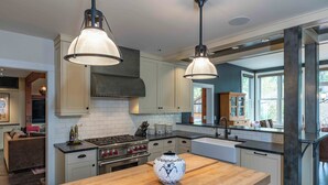 A modern kitchen with white cabinets, a wooden island, stainless steel appliances, and pendant lighting.