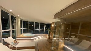 Interior moderno com banheira de hidromassagem, cadeiras de descanso e grandes janelas com vista para a cidade.