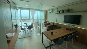 Um espaço de escritório moderno com uma grande mesa, cadeiras, uma televisão e vista da cidade através de amplas janelas.