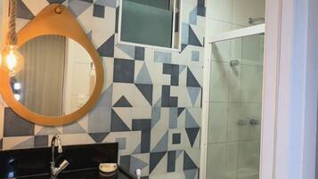 Ein modernes Badezimmer mit einem geometrischen Fliesenrückwand, einem runden Spiegel mit einer Glühbirne, einer weißen Toilette und einer Duschkabine aus Glas.