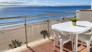 A balcony with a white table and chairs, overlooking a beach with a clear view of the ocean and distant mountains. - Agi Europa 62 Apartamento for rent in Roses Girona. (Roses)