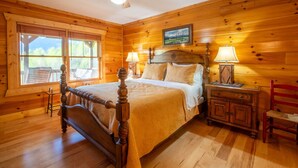 Ein Schlafzimmer in einer Holzhütte mit einem Himmelbett, zwei Nachttischlampen, einem Deckenventilator und einem Fenster mit Jalousien.