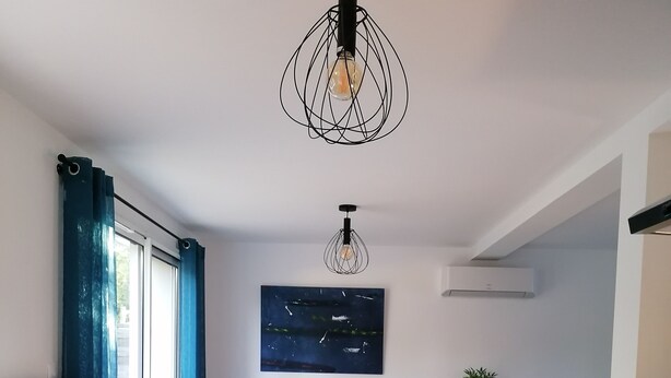 Una cucina moderna con isola in legno, un tavolo da pranzo con sedie, un lampadario e un'ampia finestra con tende blu.