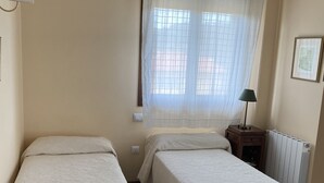 A bedroom with two single beds, a window with sheer curtains, a bedside lamp, and a radiator. - Short description of the property (San Juan de Duz)