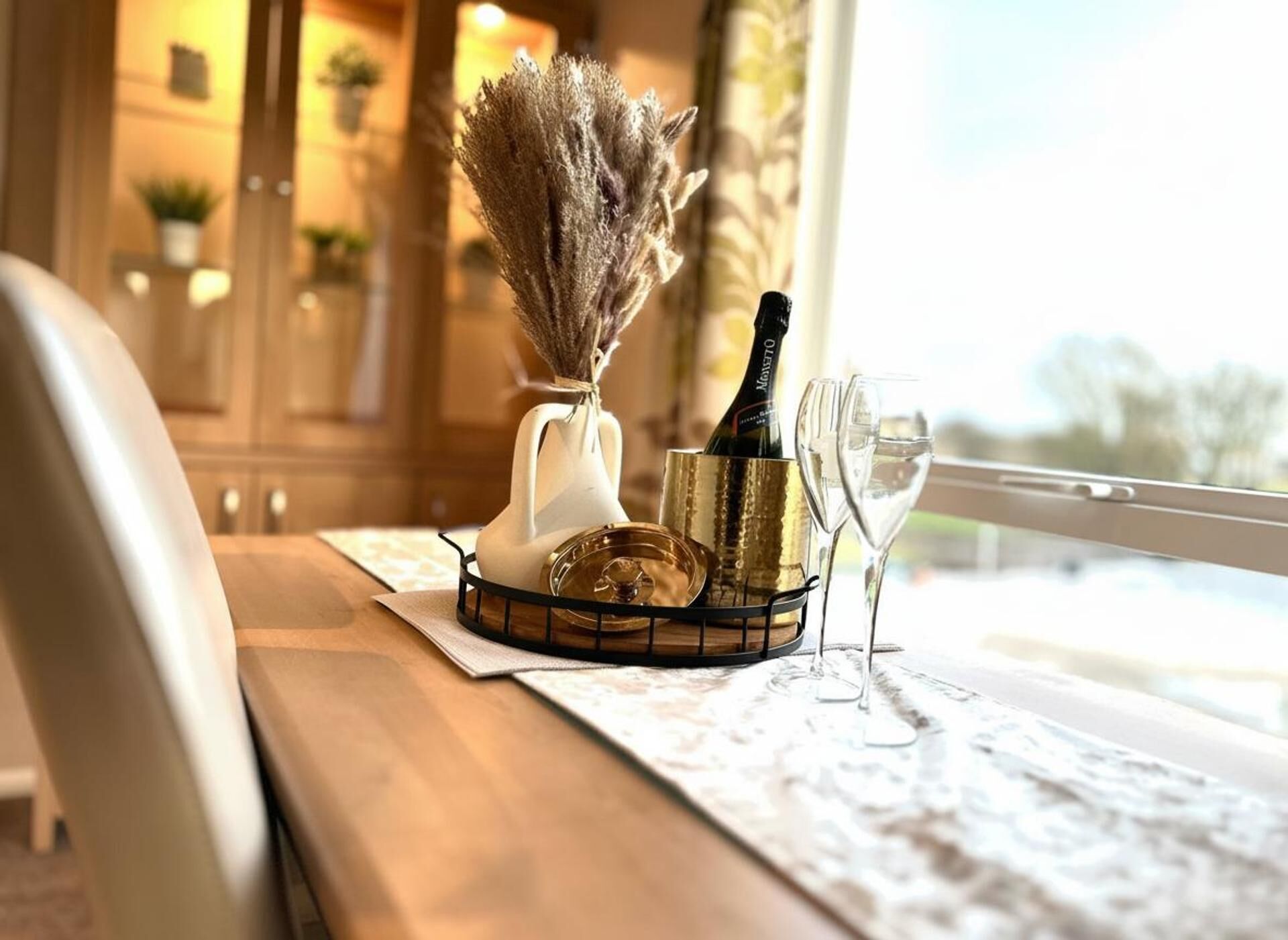 Ein Tisch mit einer Champagnerflasche, einem Glas und einer dekorativen Vase mit getrockneten Blumen.
