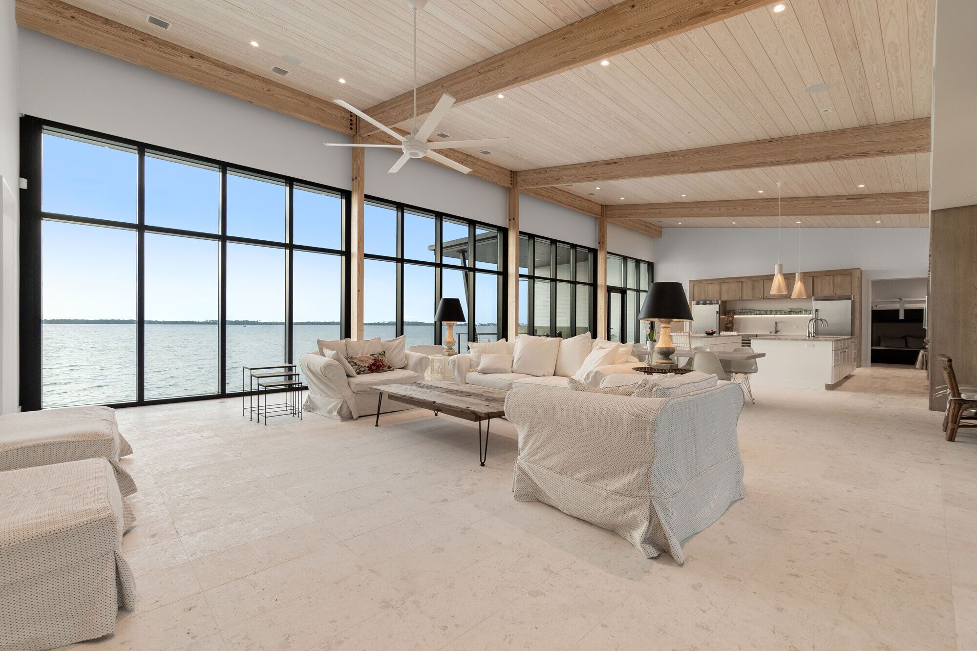 A spacious living area with large windows, a ceiling fan, and a view of the water.