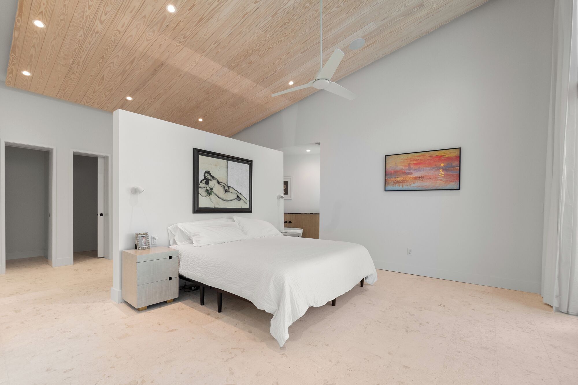 Una camera da letto con un letto, un comodino, una ventola a soffitto e opere d'arte alle pareti.