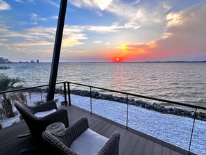 A deck with wicker chairs overlooking a body of water during sunset. - Luxury Waterfront 6 Bedroom. 6.5 Bath Home with Private Pool! (Pensacola Beach)