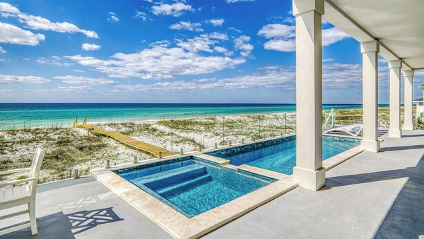 Une piscine avec une eau d’un bleu limpide, une plage de sable et une vue sur l’océan.
