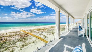 Vue sur la plage depuis un balcon abrité, avec une passerelle en bois menant à la plage.