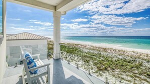 Un balcon doté d’une porte vitrée donnant sur une plage de sable blanc et une eau d’un bleu cristallin.