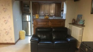 A living room with a black leather sofa, a kitchen in the background, and a radiator on the right. - Gite à la Campagne (Quins)