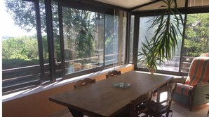 A dining area with a wooden table and chairs, large windows with a view of greenery, and a potted plant. - Gite à la Campagne (Quins)