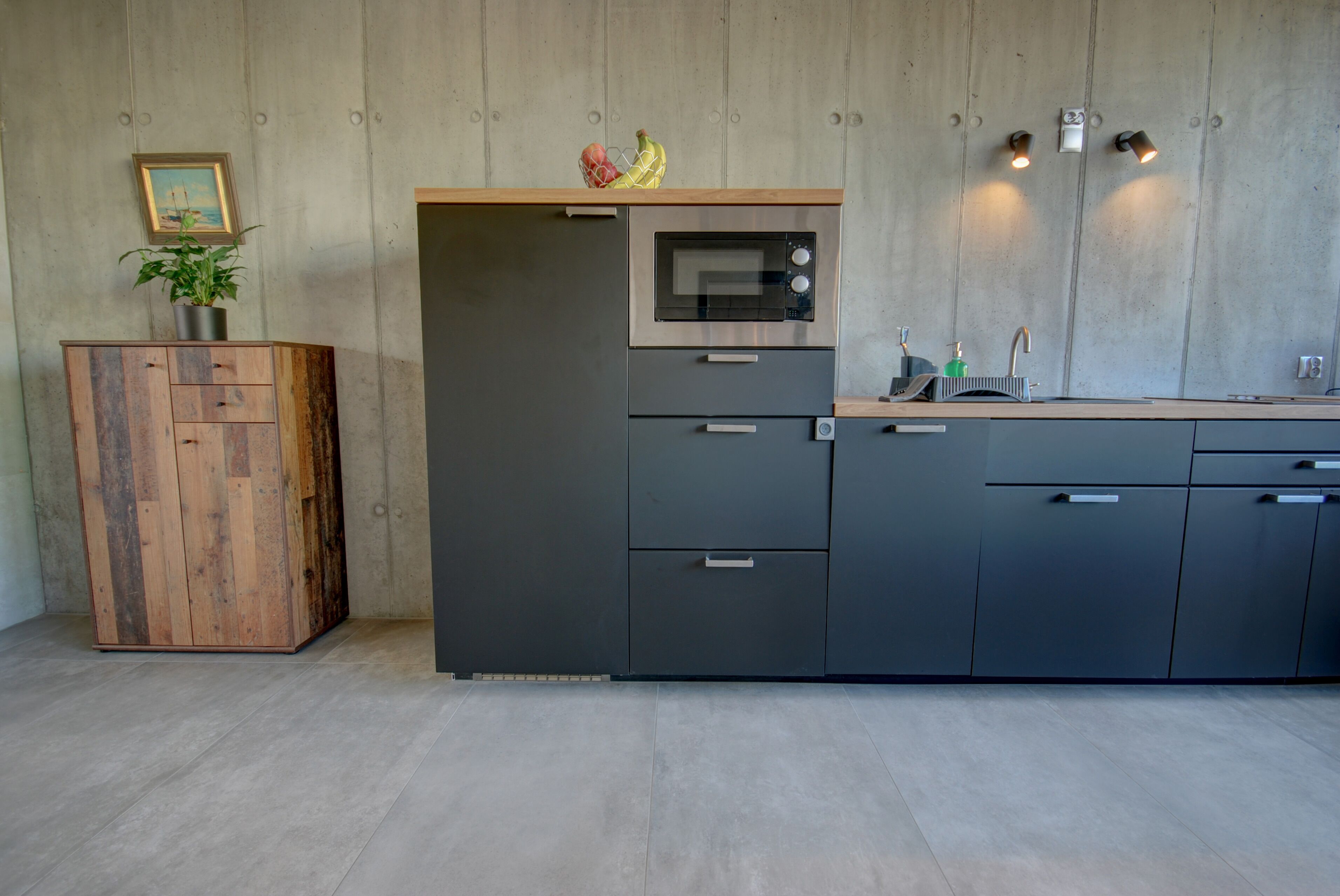 Una cucina moderna con forno a microonde integrato, un mobiletto in legno e un piano di lavoro con lavello e rubinetto.