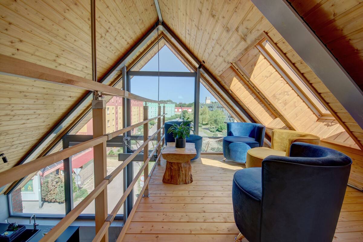 Quarto moderno no sótão com teto inclinado, janelas amplas e vista para a cidade.