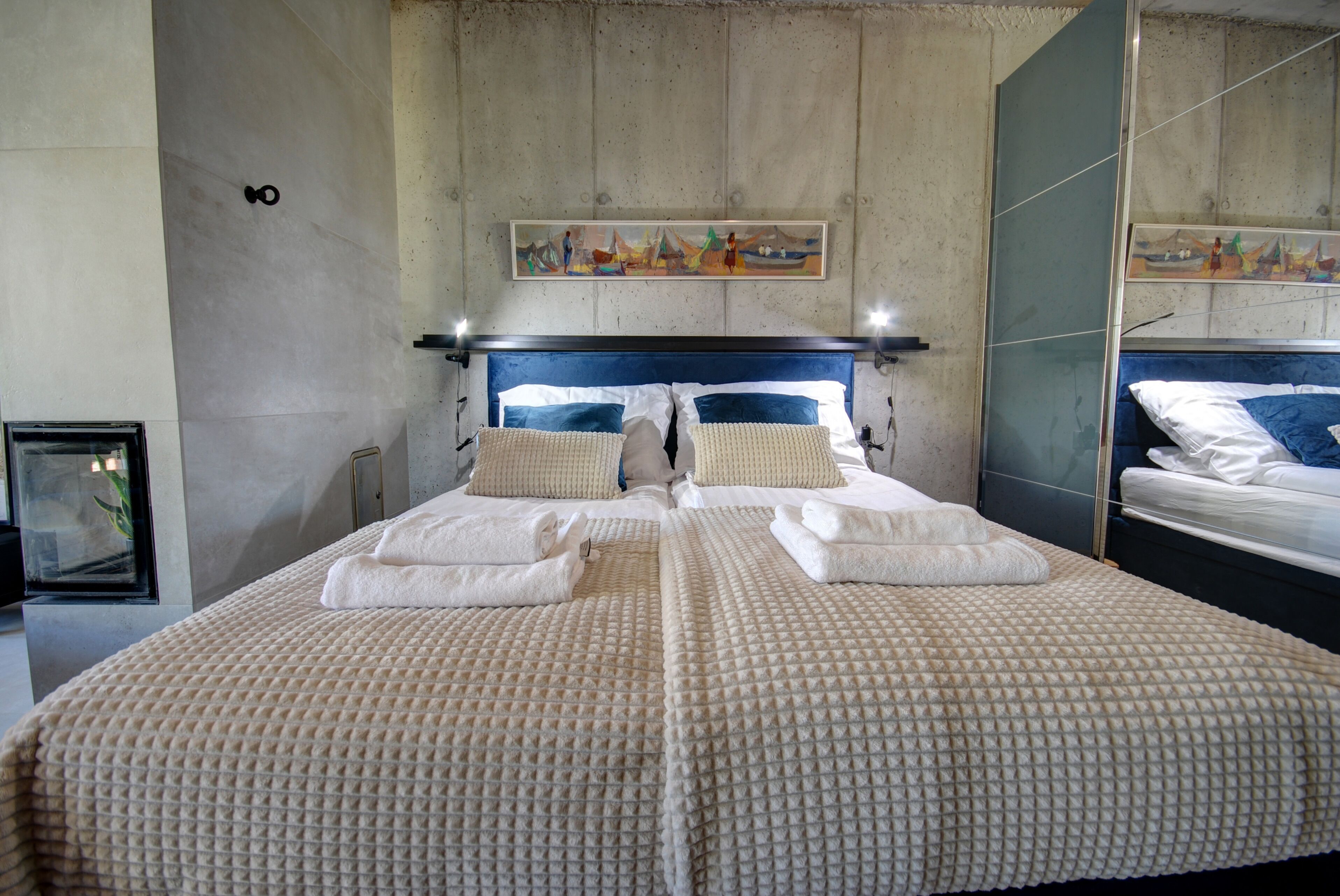 A double bed with a textured beige cover, two pillows, and neatly folded towels.