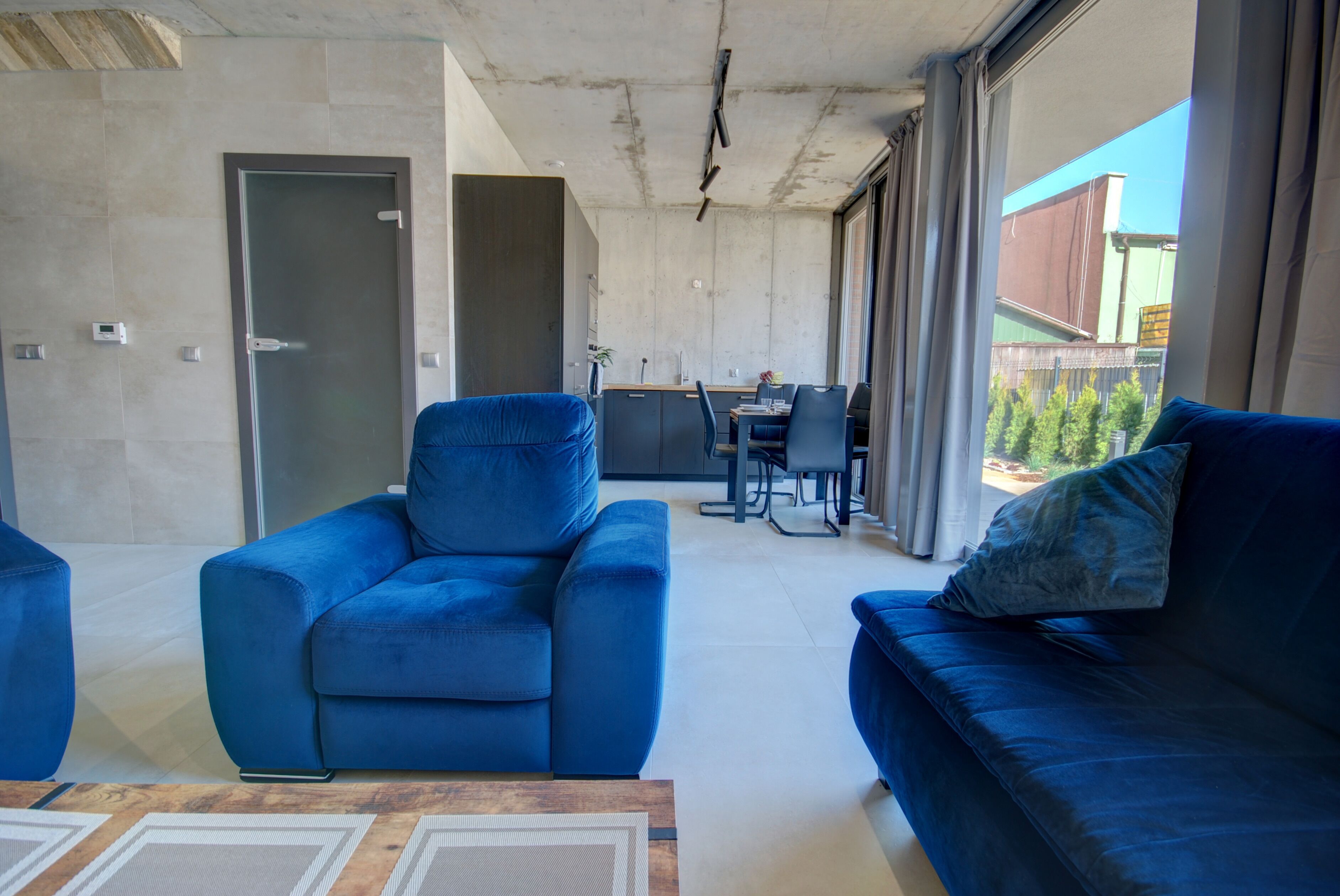 A modern living room with a blue sofa, a wooden coffee table, and a dining area in the background.